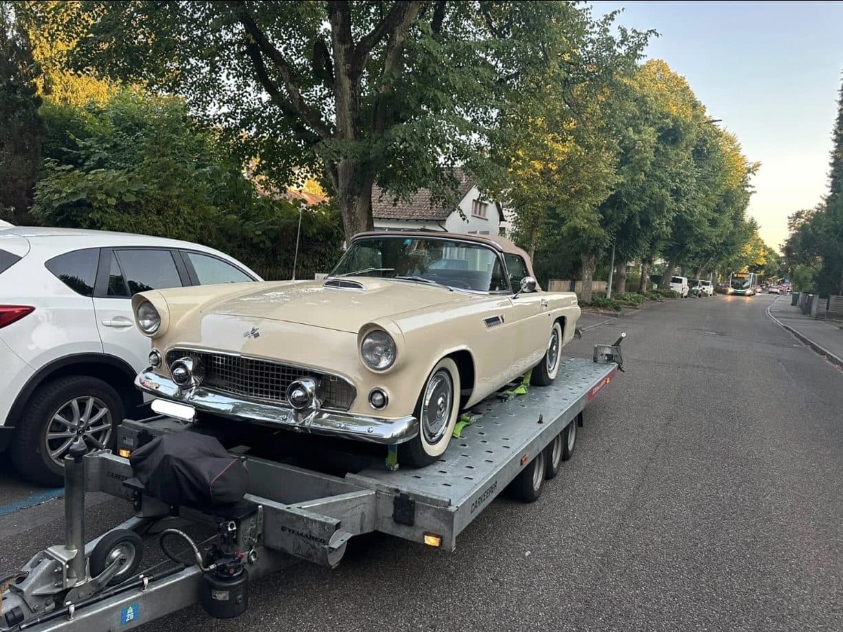 Cremefarbenes Oldtimer-Cabriolet auf dem Anhänger in einer Allee