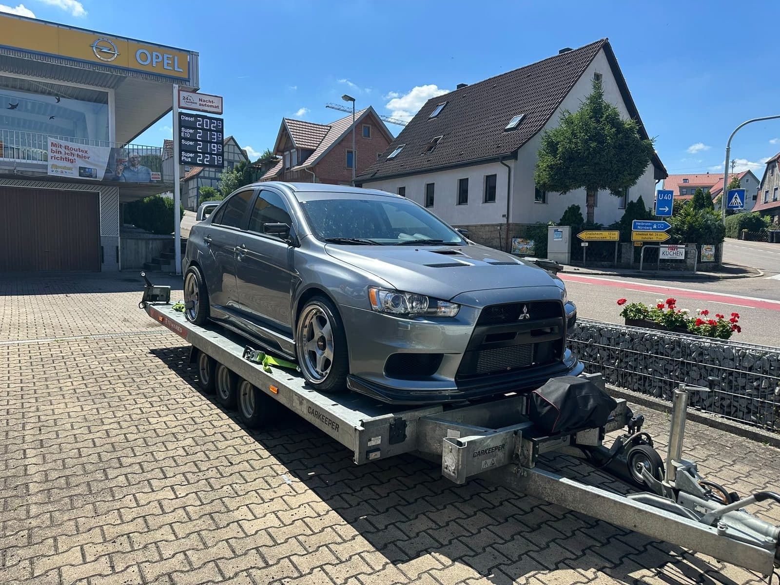 Tiefergelegter grauer Mitsubishi auf dem Anhänger vor einer Tankstelle